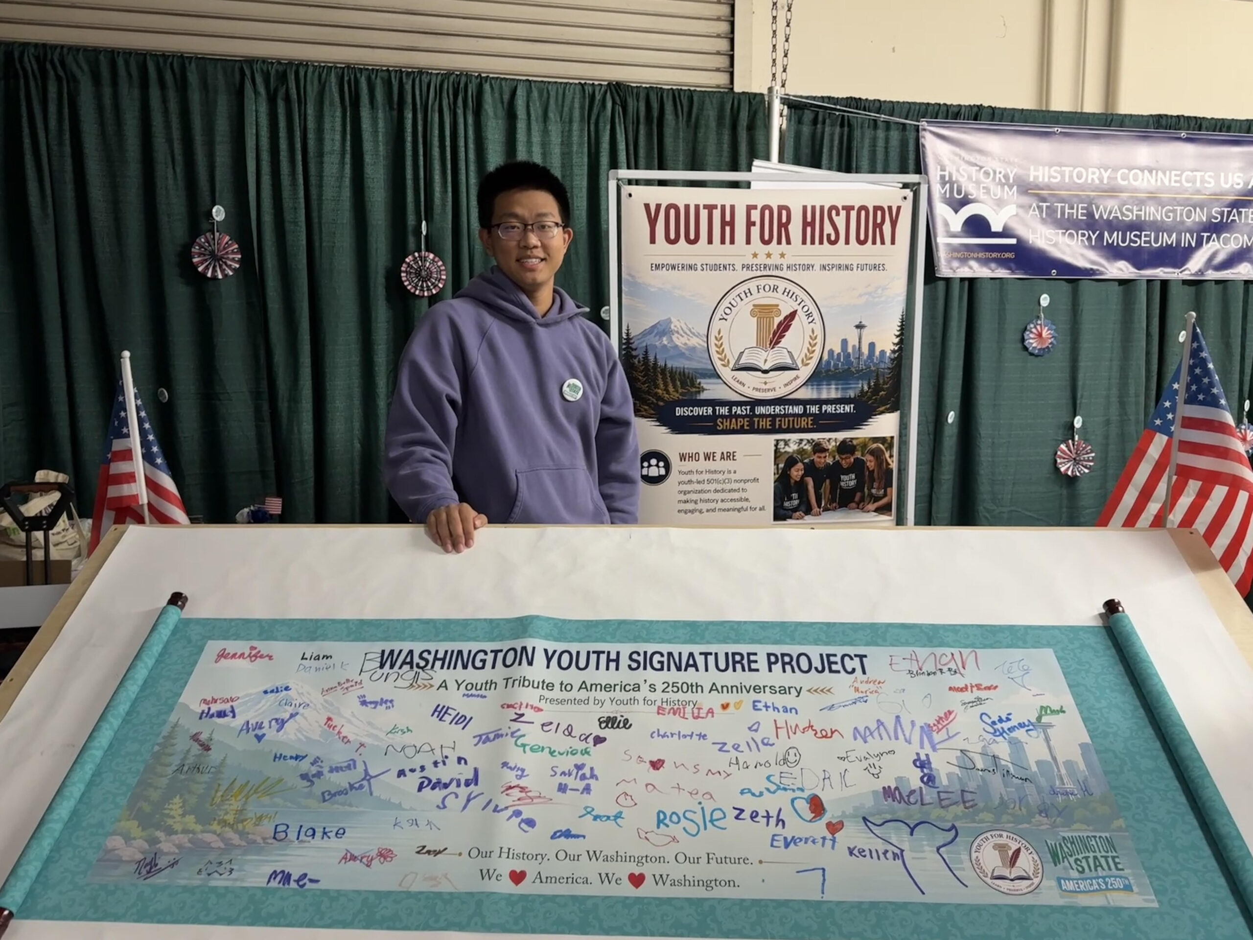 A Youth for History volunteer stands behind the Washington Youth Signature Project banner, covered with colorful signatures.